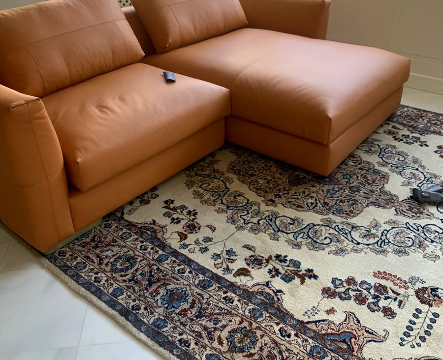 Divano angolare in pelle color cuoio su un tappeto persiano, posizionato dopo il trasloco